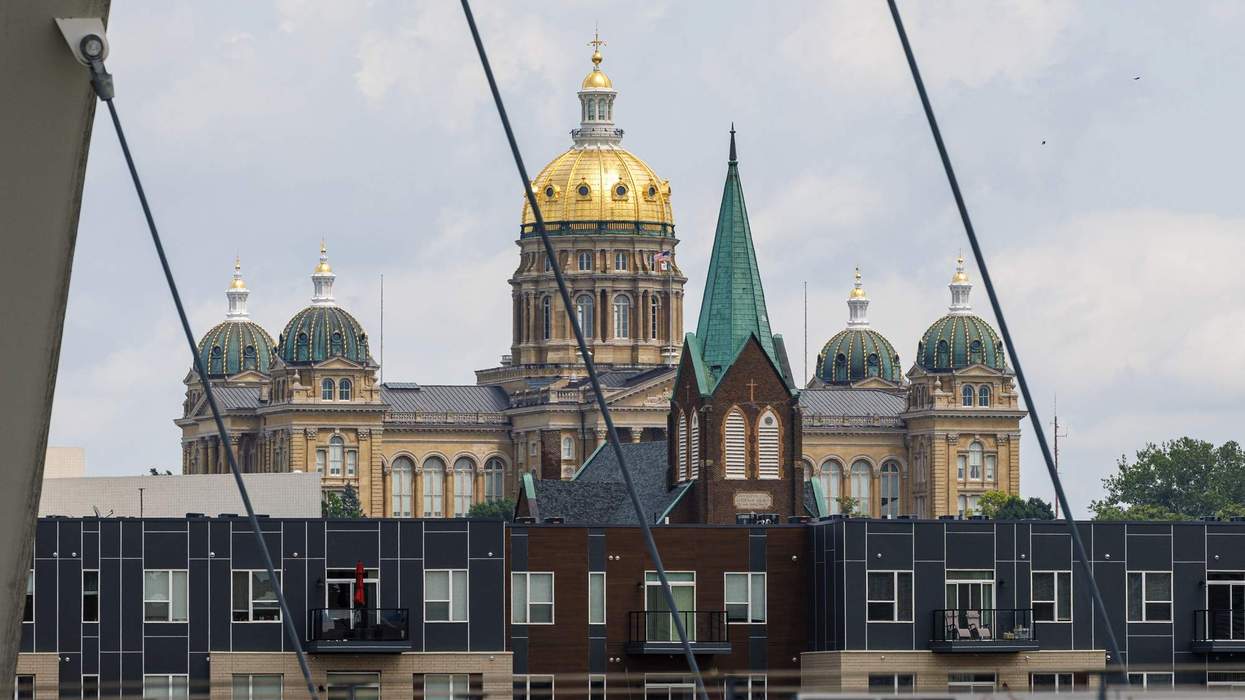 the-golden-dome-of-the-iowa-state-capitol-is-visible-through-wire-slats-on-a-suspension-bridge-over-a-river-in-front-of-the-cap